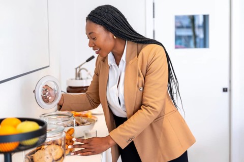 Businesswoman taking cookies from glass jar at hotel buffet, enjoying breakfast during her business