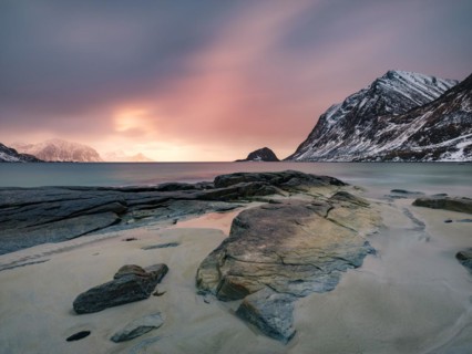Rocks on Haukland beach in the evening light, snow-capped mountains in the background, Vestvågøya,