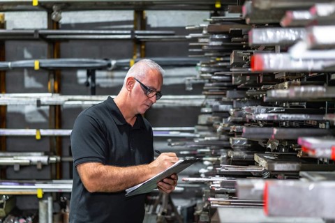 Side view photo of a mature caucasian man checking metal bars while doing inventory using a