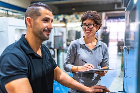 Male manual worker talking with female manager while using computer in the factory