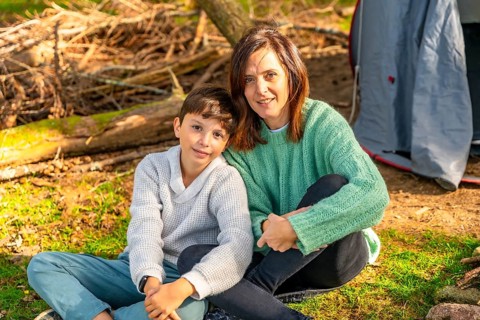 Caucasian mother and son smiling at camera sunbathing enjoying nature in the forest next to camping