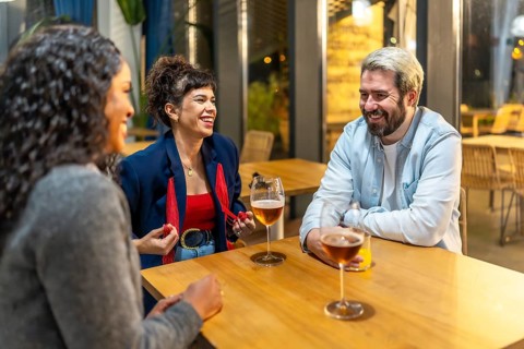 Multiracial friends enjoying night talking and drinking beer and cocktail in a bar terrace