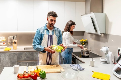 Man holding lettuce and woman cooking in a modern kitchen, preparing a healthy meal together
