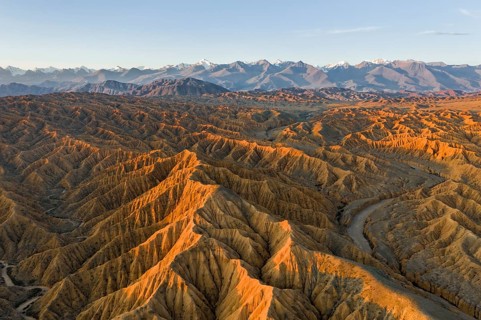 River bed runs through a landscape of eroded hills, badlands at sunset, mountain peaks of the Tian