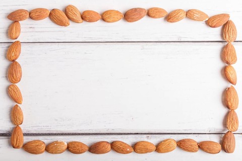 Rectangular frame made from almonds on white wooden background, flat lay. top view