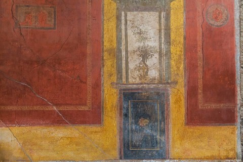 Close-up of reddish brown, blue and white frescoes on yellow wall of old residential building at