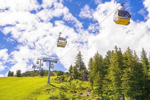 Several cable cars travelling across a green meadow under a cloudy sky, Penken, Zillertal, Austria,