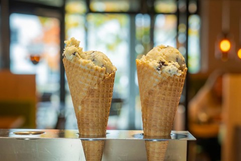 Two ice cream cones in the foreground in front of a warm café ambience with glass windows and soft