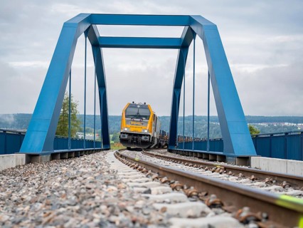 Yellow train on blue bridge over rails on a cloudy day, track construction, rail delivery for