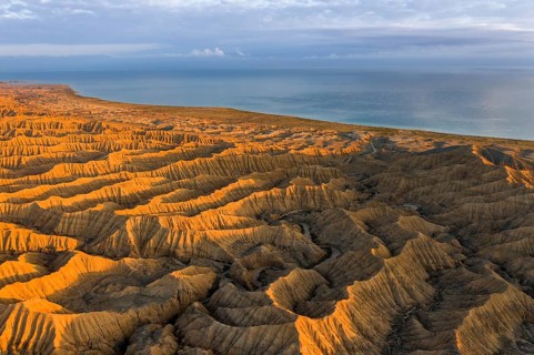 Landscape of eroded hills, badlands at sunset, Lake Issyk Kul in the background, aerial view,