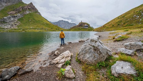 Mountaineer in yellow jacket at the mountain lake, view over the Wolayersee lake to the alpine club