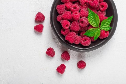 Fresh raspberries, on a black plate, with leaves, top view, on a white table