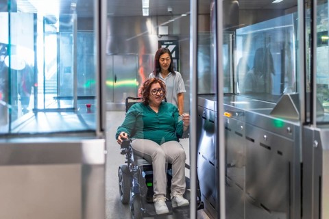 Disabled woman in electric wheelchair and chinese friend entering to the metro station