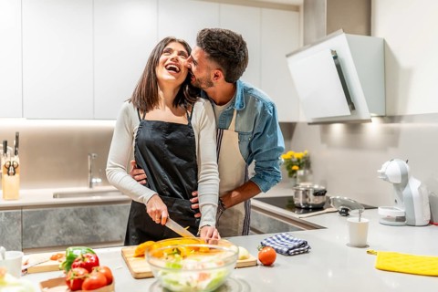 Young couple having fun while preparing a healthy meal together in their modern kitchen, enjoying