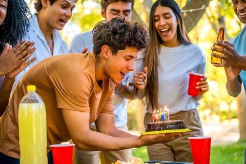Happy young man with with birthday cake celebrating with friends at park