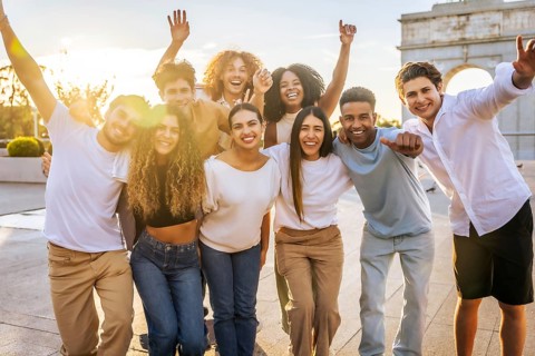 Portrait of diverse group of cheerful young people having fun and raising arms while standing