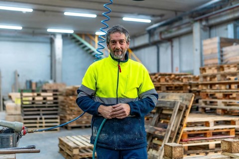 Portrait of a mature man manual worker with reflective clothes in a recycling plant full of pallets