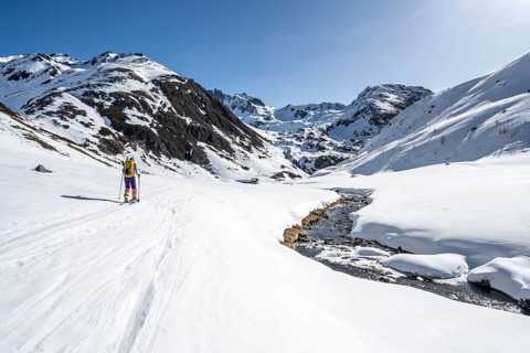 Ski tourer in the snow by a mountain stream in the Funtauna Valley, Graubünden Haute Route, Albula