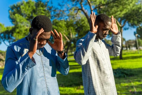 Two young senegalese men wearing traditional dashiki clothing are praying outdoors in a park,