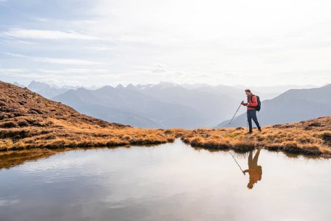 Mountaineer hiking with poles, reflected in a small mountain lake on the Krahberg, mountain