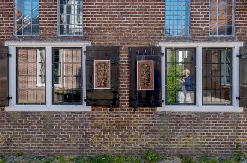 Facade of a brick building with mullioned windows and dark shutters, reflections in the glass,