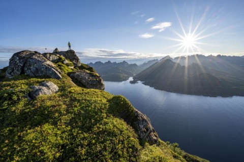 Mountaineer on the summit of Dronningsvarden or Stortinden, behind sea and fjord Umvågsundet,
