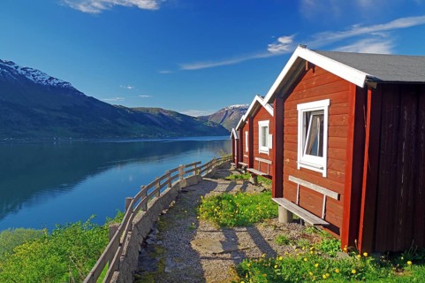 Red wooden cabins on a campsite, view of the fjord and mountains, Hardangerfjord, Fylke Vestland,