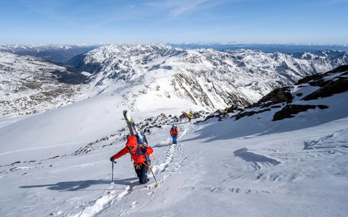 Ski tourer on foot, carrying skis on backpack, mountain panorama, snow-covered mountain landscape