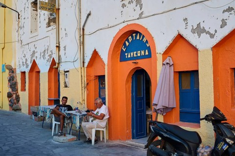 People sitting in front of a colourful facade of a taverna and enjoying their time on the street,