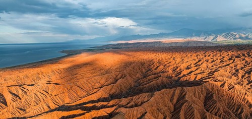 Landscape of eroded hills, badlands at sunset, Issyk Kul Lake in the background, aerial view,