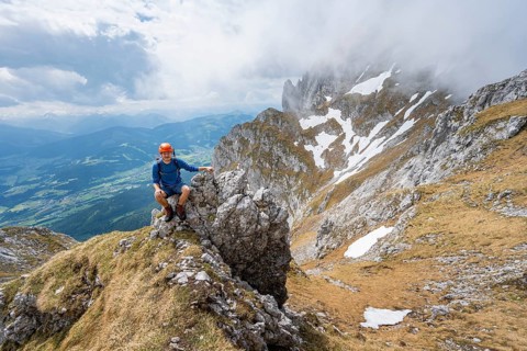 Mountaineer with helmet sitting on a rock, ascent to the Maukspitze, clouds moving around the