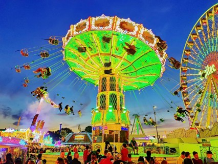 The colourfully illuminated Wellenflug chain carousel and the Ferris wheel in the evening, Cranger