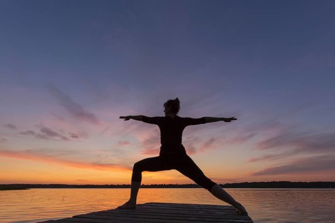 Woman practicing yoga posture Virabhadrasana II, Warrior Pose, lunging standing asana on jetty at