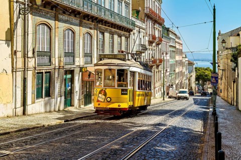 A historic yellow tram travels down a sunny Lisbon street lined with old buildings under a clear