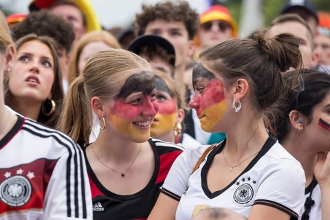 Women wearing make-up in the German national colours watch the football match in the fan zone at