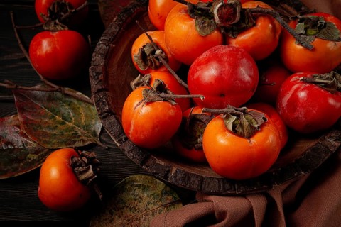 Fresh persimmon, in a wooden plate, top view, no people