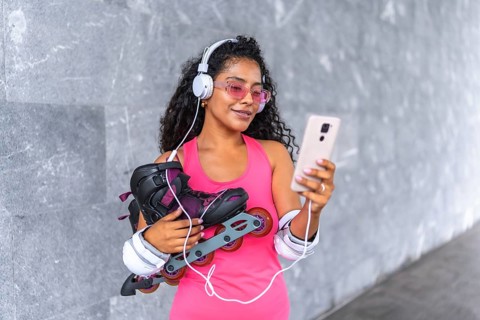 Latin beauty woman with inline skates listening to music with mobile phone and headphones at urban