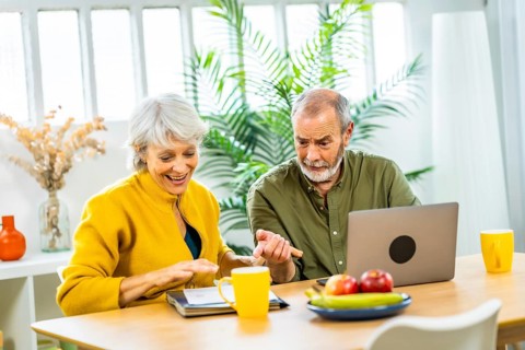 Caucasian casual and happy senior couple at home planning home budget together using laptop
