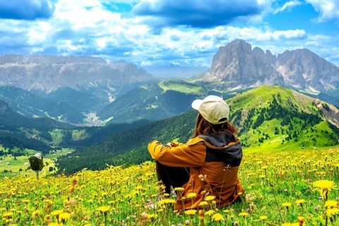 Woman hiker sitting in a vibrant flower field, admiring the stunning seceda peaks rising