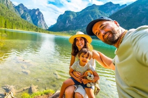 Happy family taking a selfie by the transparent water of lake dobbiaco with the dolomites in the