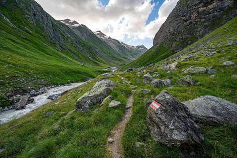 Hiking trail in the Umbaltal valley with Isel mountain stream, glaciated mountain peaks behind,