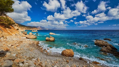 Quiet beach with large rocks framed by deep blue water and a wide sky, Kato Lakkos Beach, still