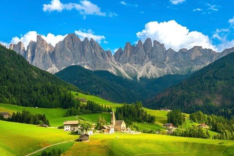 Green meadows, pine forests, and the iconic odle mountains rising majestically behind the church of