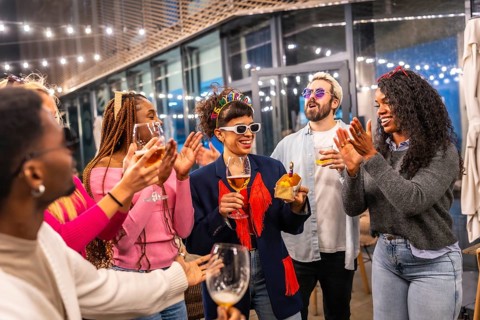 Multi-ethnic friends clasping and singing birthday song to a woman standing outside a night bar
