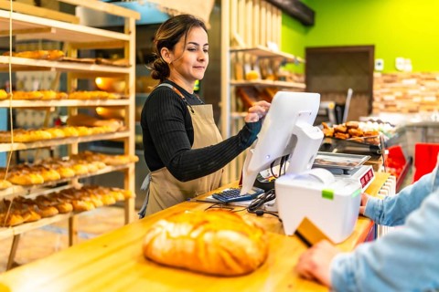 Friendly young latin saleswoman preparing the checkout for a client in an artisan bakery