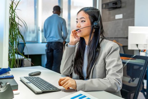 Young asian manager working diligently at a computer, wearing a headset in a sleek, modern