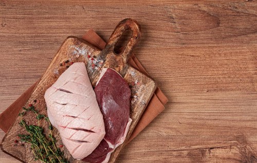 Fresh raw duck breasts, on a wooden chopping board, with herbs and spices, no people