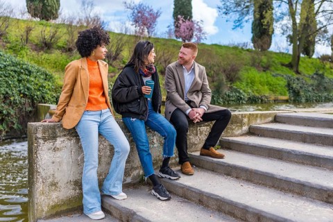 Three young professionals enjoying a conversation and coffee by a canal after work, representing