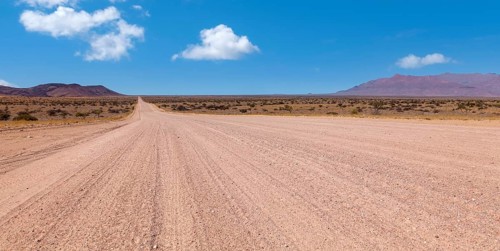An endless desert road under a blue sky with a wide, dry landscape and mountains in the background,