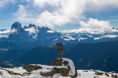 Snow-covered mountains under a blue sky with clouds and a wooden signpost with a view of the